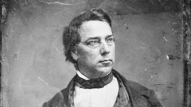 historic black and white photo of an adult man with glasses in a suit 