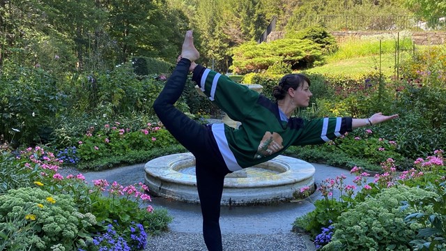 Woman in NPS arrowhead jersey stands in dancer pose in front of formal garden