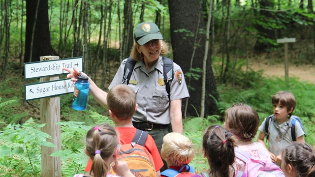 Park Ranger surrounded by young children points to sign that says "Stewardship Trail" 