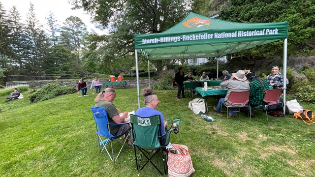 group of people in lawn chairs near tent with park name and arrowhead logo