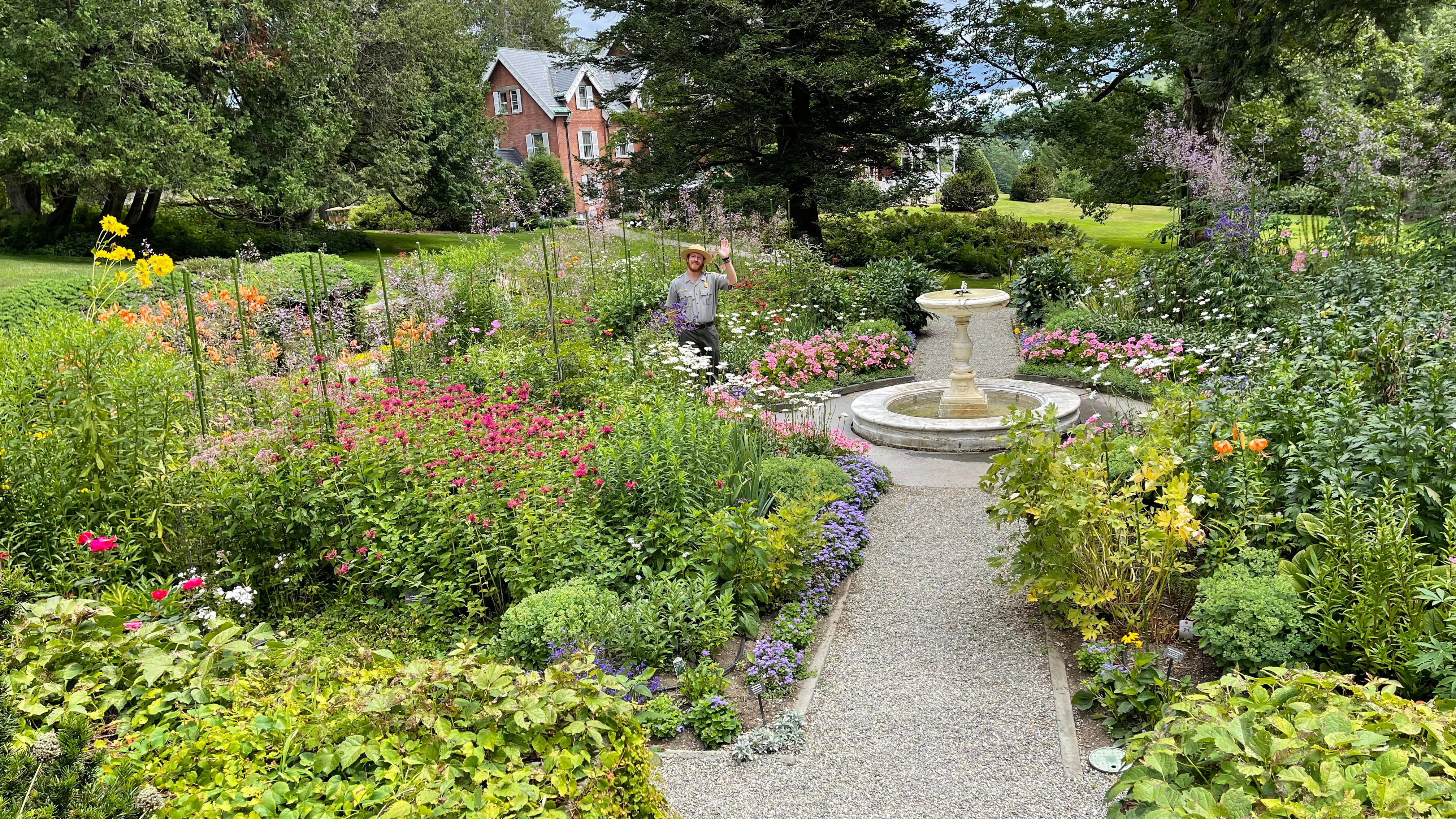 park ranger waves at camera from formal four square garden