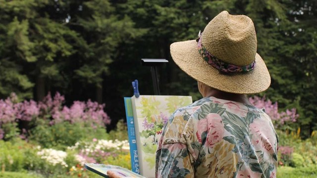artist paints in garden with back turned to camera