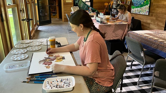 photo of person watercolor painting with another artist working in the background