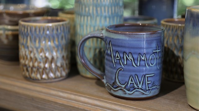 Handcrafted, clay mugs sit on a retail store shelf, ready for sale.