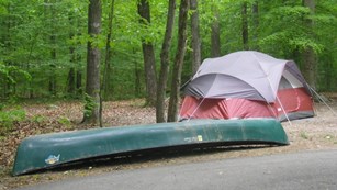 A tent set up in a campground with a canoe sitting next to it. 