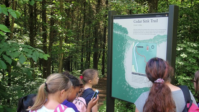 Group of hikers reads a trail information board near the Cedar Sink trailhead.