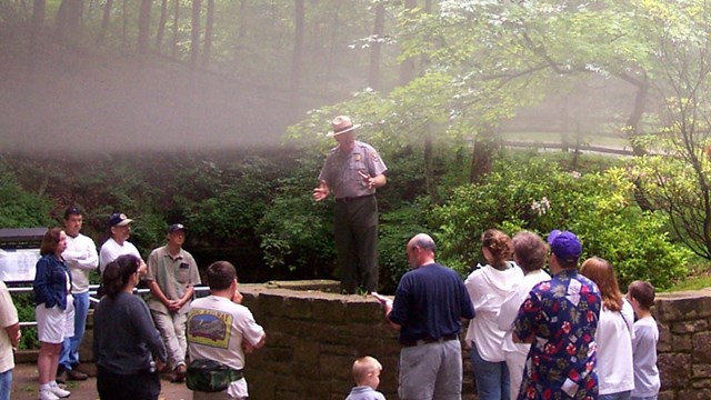 Fog descends as a park ranger addresses a group above the large Historic Entrance  of Mammoth Cave.