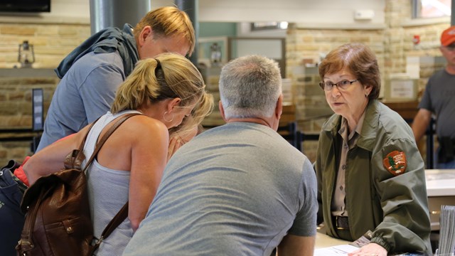 A ranger talks to a small group of 3 people at an information desk.