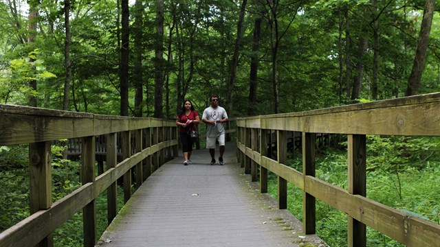Two people walking on a wooden boardwalk. 