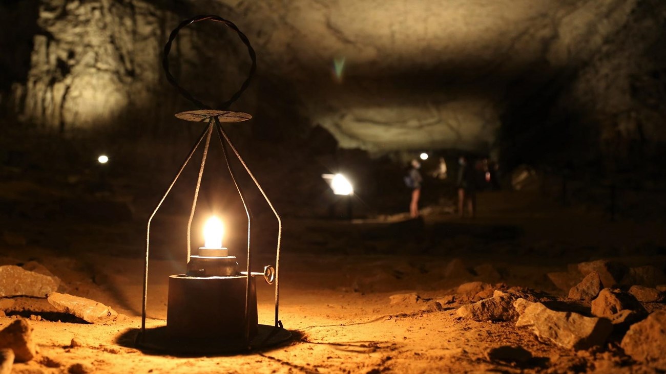 An open flame wire lantern in a large rocky and dark cavern.