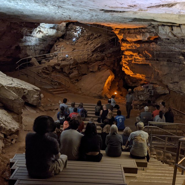 A group of people sitting on benches in the cave. 