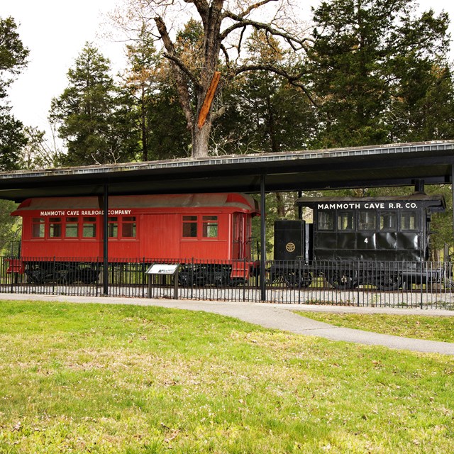 Two historic train cars sitting under a open air shelter. 