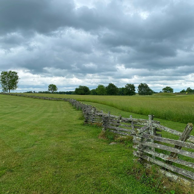 A large open field with a old wooden fence running down the middle. 