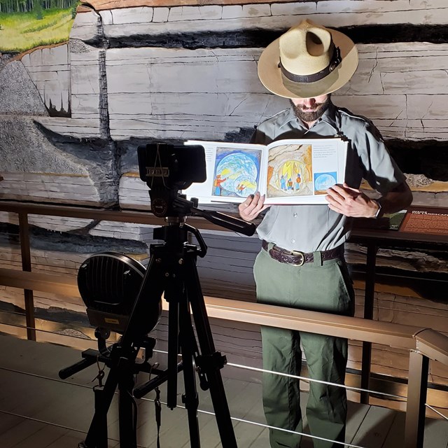 A park ranger holding a book with a camera facing them in the foreground