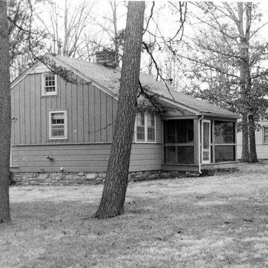 A black and white photo of small houses surrounded by trees. 