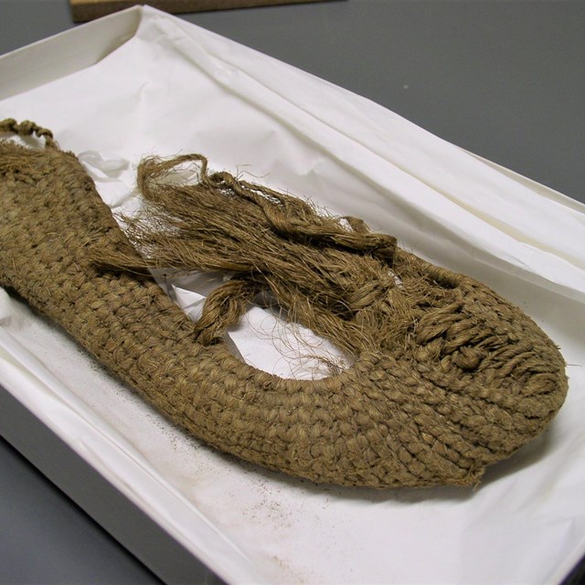 A woven slipper laying on a white tray. 