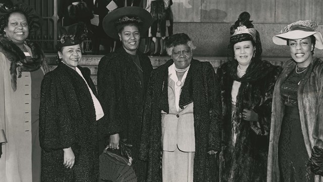 Image of Mary McLeod Bethune and five other women standing outside in front a building wearing coats