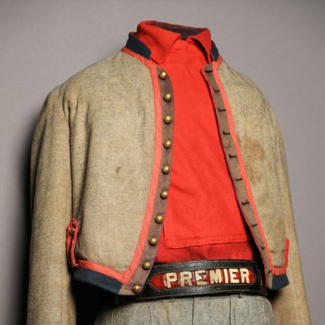 Color photo of Francis Brownell Uniform. Khaki colored jacket, orange collared shirt, belt. 