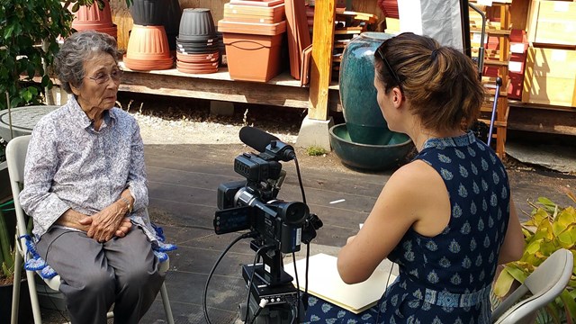 Image of elderly woman being interviewed on camera, background in flower shop