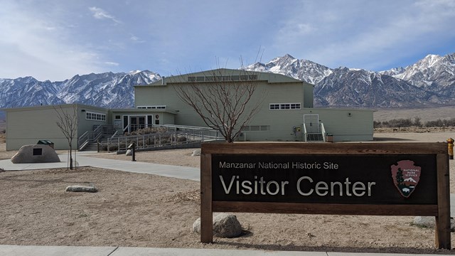 Foreground Visitor Center sign, background faded green auditorium in front of snow capped mountains