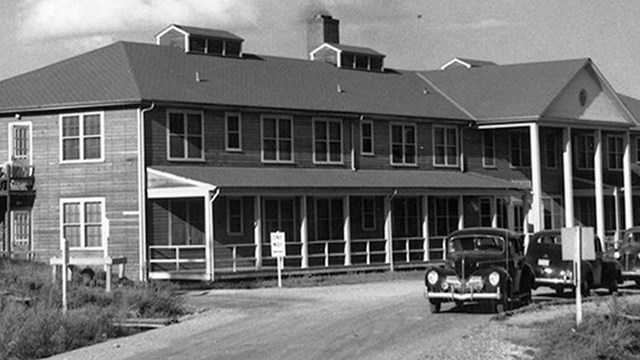 Black and white photo of a hotel with several cars at the front.