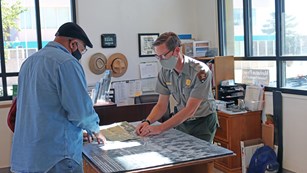 A park ranger points out something on a map to a visitor.