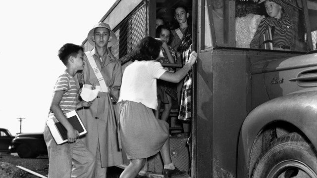 Historic image of 3 students climbing into a bus with 6 more students already on it. 