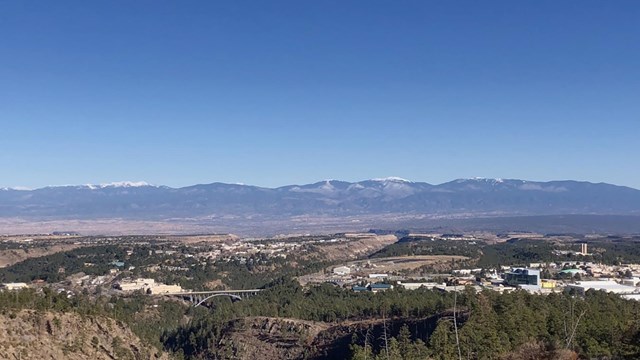 Color photo of urban areas, forest and mountains taken from a high vantage point.