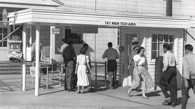 Black and white photo of a people entering a building that reads "Technical Area."