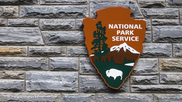 An arrowhead that reads "NPS" on a stone wall. 