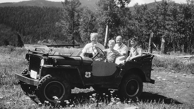 A black and white photo of two older men and two children driving a Jeep.