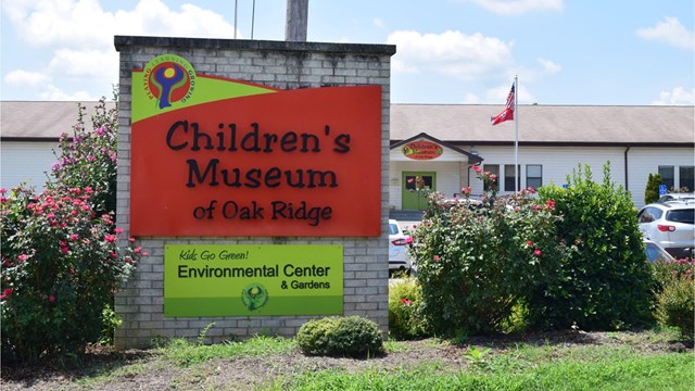 A large sign in front of a parking lot and school building.