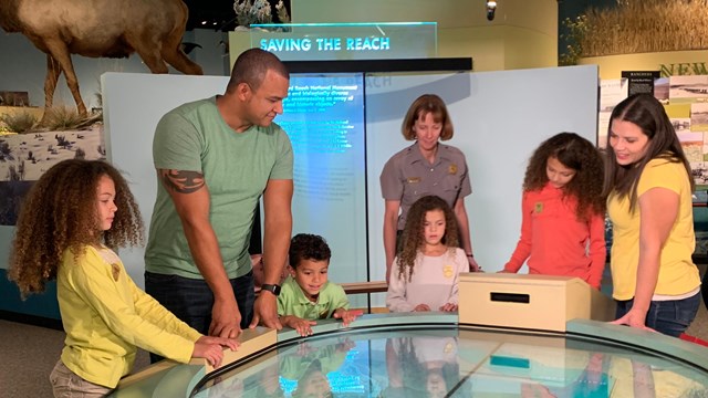 Photo of a group of three adults and four children looking at a round exhibit.