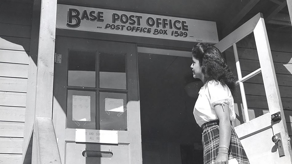 A black and white image of a woman going to a post office box, with a sign that reads, "PO Box 1889"
