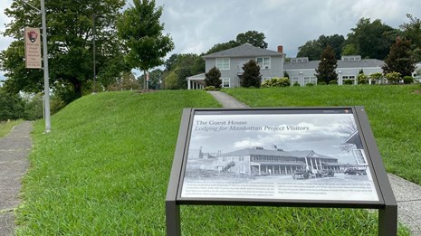 A large hotel-type structure on a grassy hill with an historical marker in the foreground. 