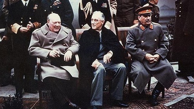 A color photo of three men in seats with others standing behind them. 