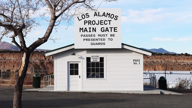 Small white building with a sign that reads "Los Alamos Project Main Gate."