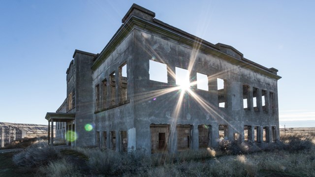 As the sun goes down, it shines through an old gray building with no windows and nothing inside of i
