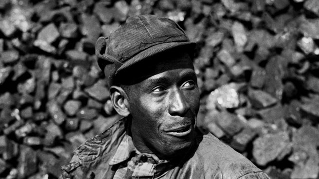 A black and white photo of a black man standing at a podium in front of a large group of black peopl