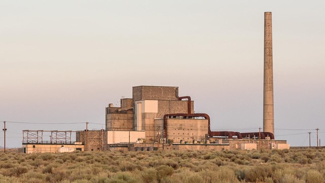 A color photo of a blocky building with a ventilation stack in a bushy, treeless field.