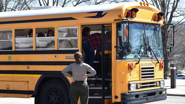 School bus parked with a uniformed ranger standing at the open door.