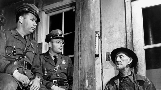 A black and white photo of two men in uniform talking to an older man. 