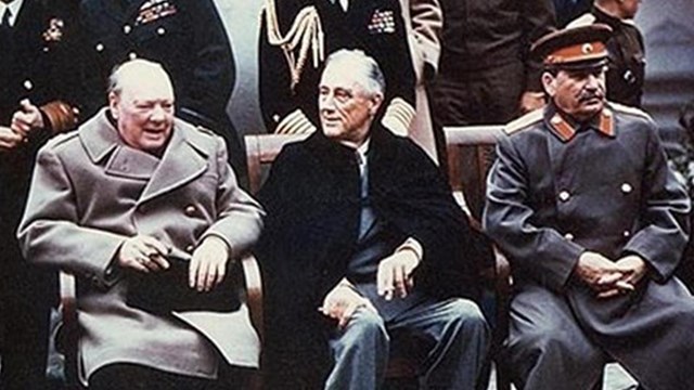 Three men sit in chairs at a conference.