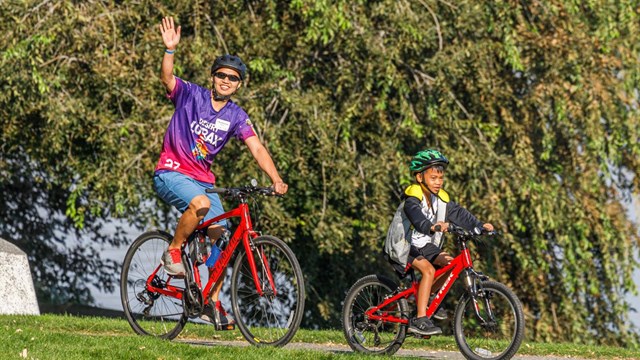 A color photo of a man and child riding their bikes. 