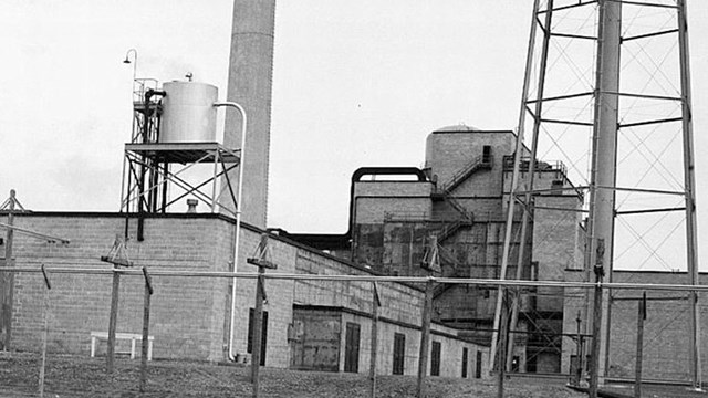 An industrial facility with a water tower and smokestack.  