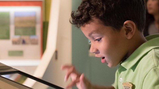  A young boy presses on an interactive screen in a museum. 