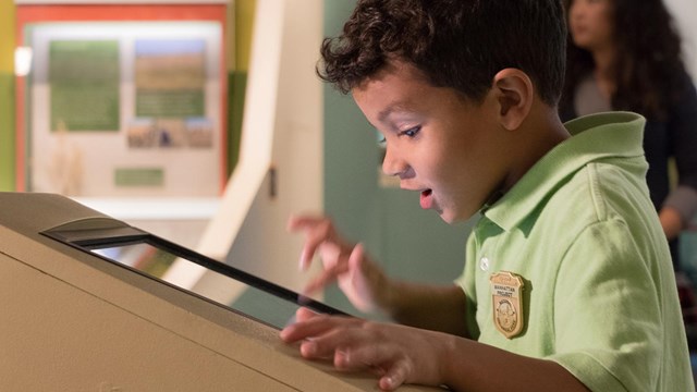 A kid in a green shirt touches a screen with an excited face.