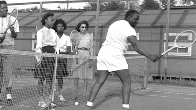 Several men and women playing tennis on an outdoor tennis court.