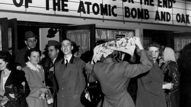 Several people gather in front of a movie theatre. 