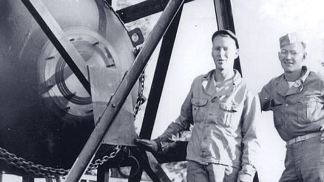 Two men stand next to a large metal orb.